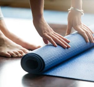 Close-up of attractive young woman folding blue yoga or fitness mat after working out at home in living room. Healthy life, keep fit concepts. Horizontal shot